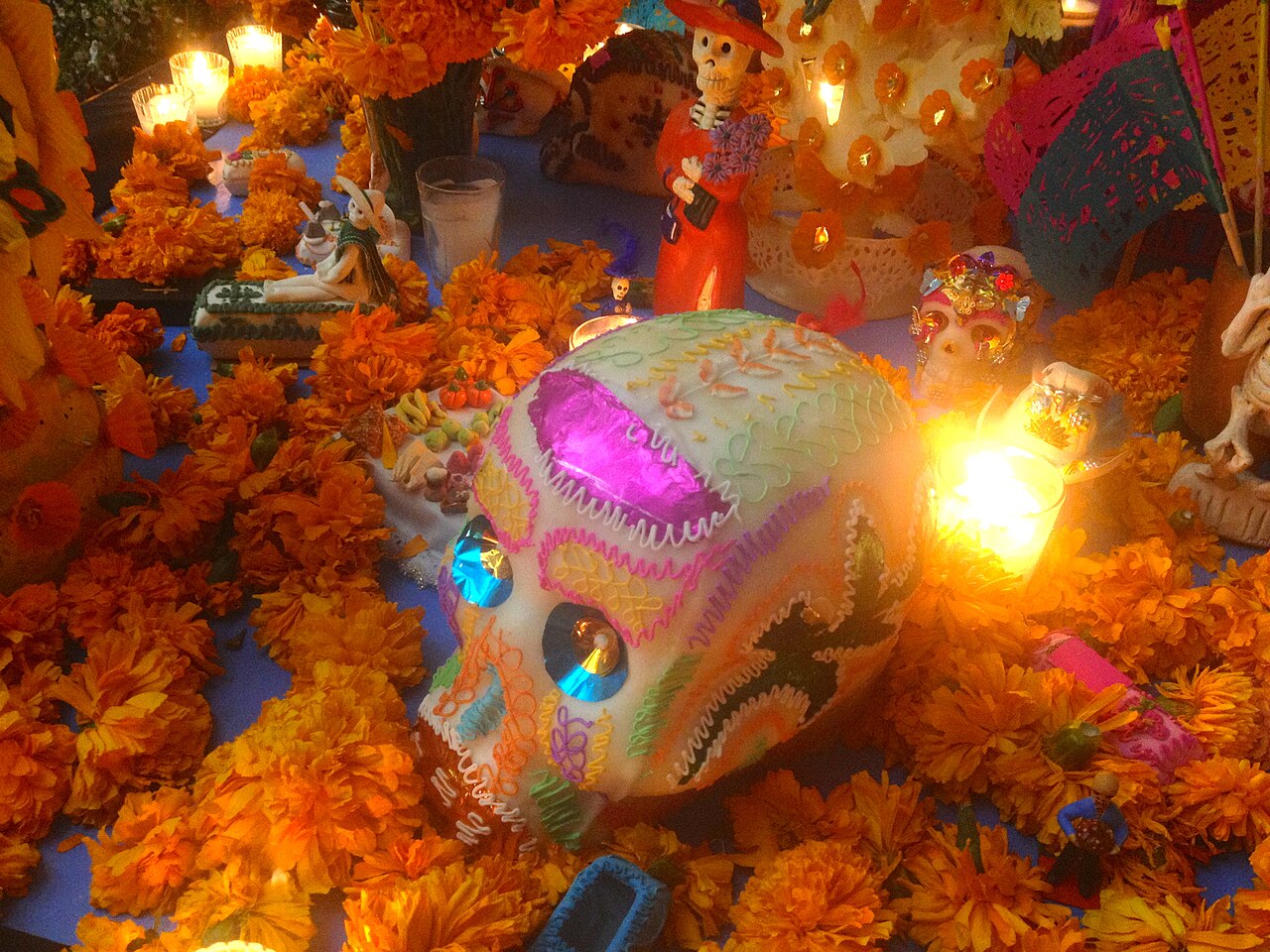 Calavera de azúcar artesanal, catrina y flores naranjas de cempasúchil iluminadas por velas en la ofrenda del Día de Muertos